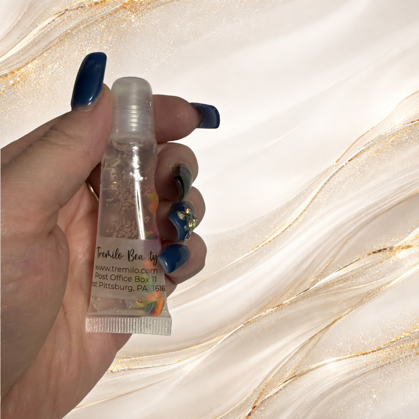 Hand holding a 10 ml Paradise Fruit™ Tremilo lip gloss in a clear squeeze tube with floating fruit slice charms