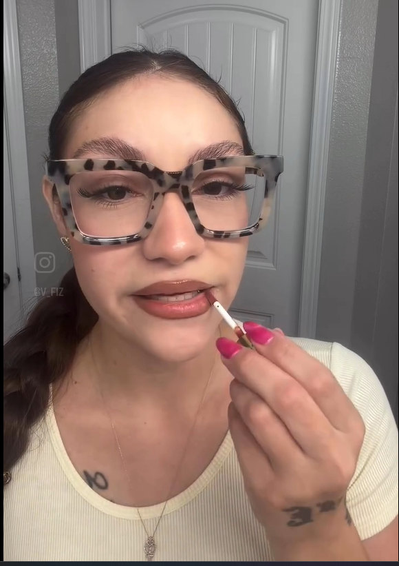 Person applying lipstick with a neutral background