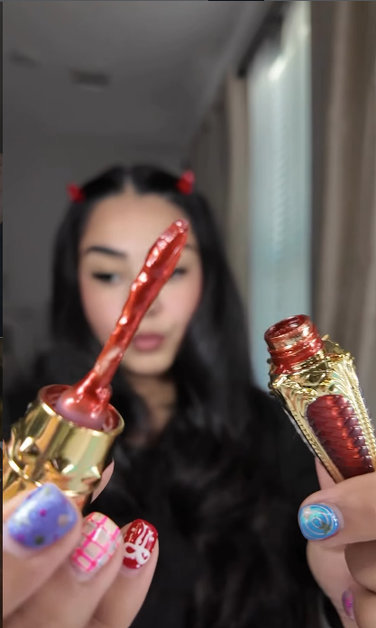Close-up of two decorative lipsticks held by a person with colorful nails.