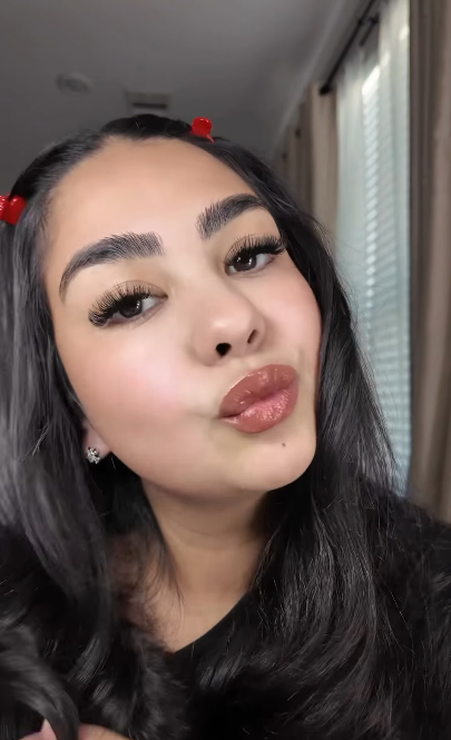 Woman with long dark hair and red hair clips blowing a kiss indoors.