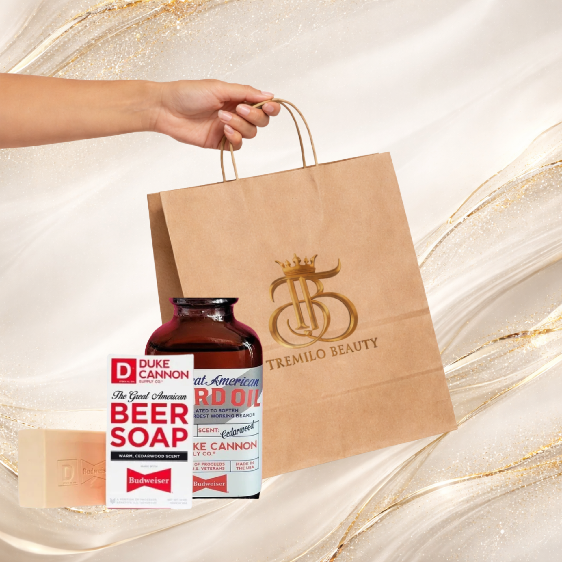 Gift bundle from Tremilo Beauty featuring a kraft paper shopping bag, men’s beer soap, beard oil, and a shower bomb, held by a hand on a white and gold background.