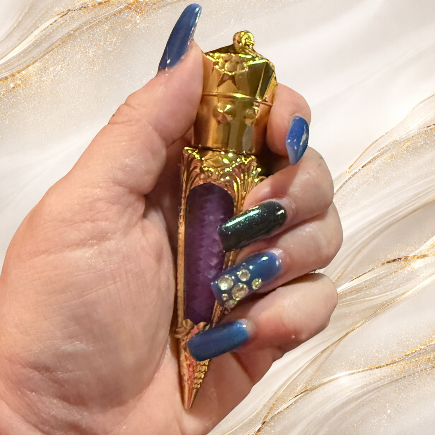 Hand holding Violet Confluence lip gloss in gold claw tube showing purple shimmer by Tremilo Beauty