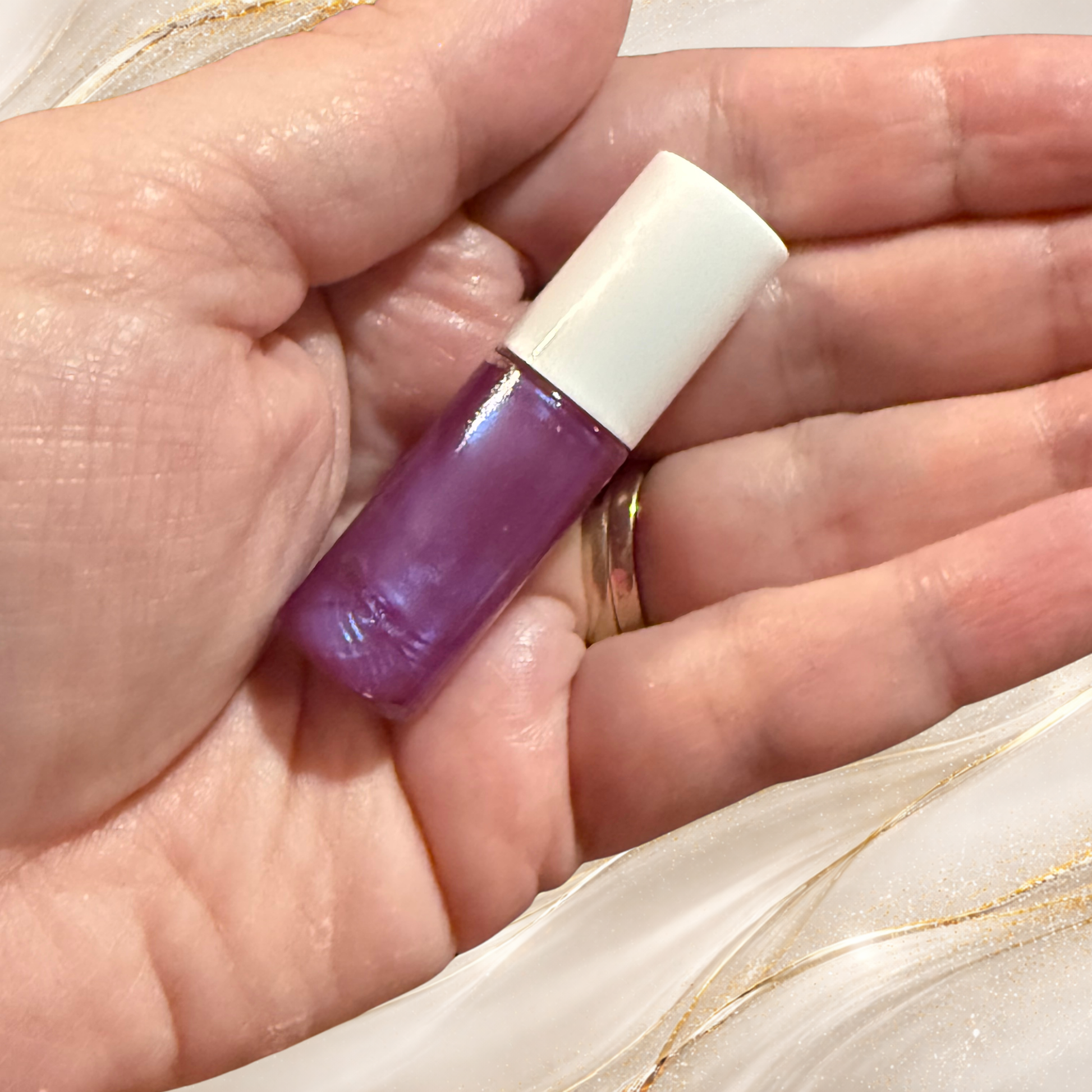 Hand holding Violet Confluence mini lip gloss tube with purple shimmer by Tremilo Beauty
