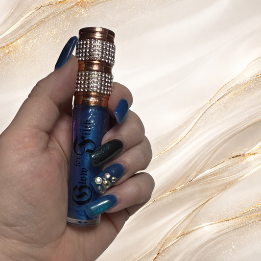 Blue Alchemy lip gloss by Tremilo Beauty held in hand featuring shimmering sapphire blue gloss with rhinestone cap.