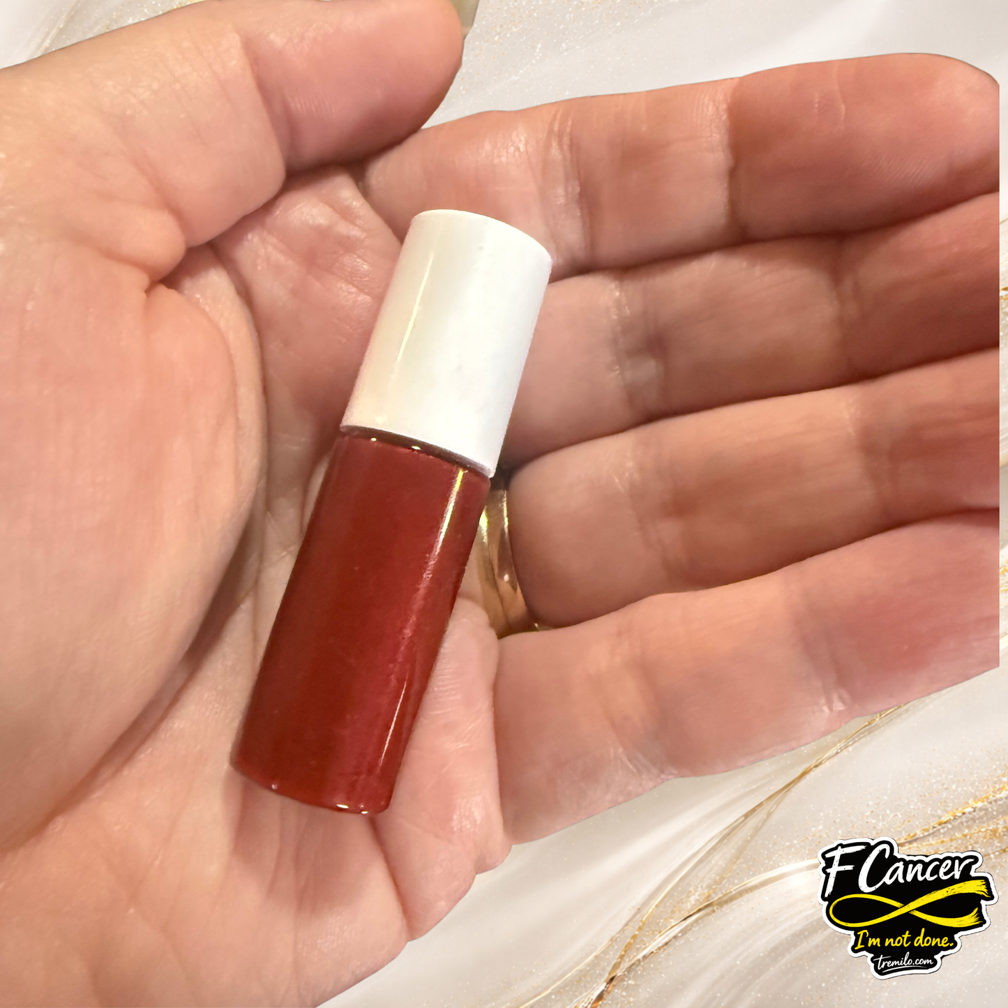Hand holding F Cancer 3ml lip gloss by Tremilo Beauty showing compact size and red gloss color