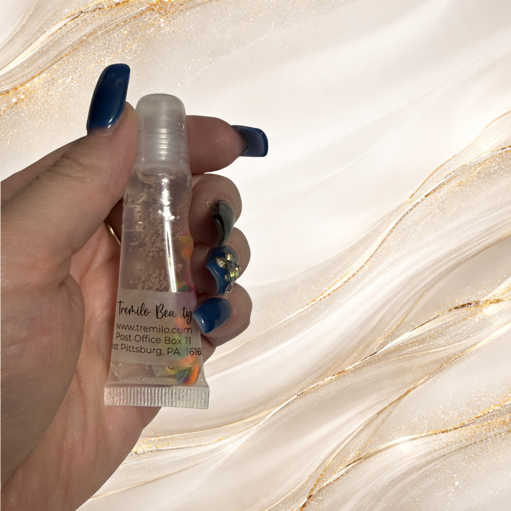 Hand holding a 10 ml Paradise Fruit™ Tremilo lip gloss in a clear squeeze tube with floating fruit slice charms
