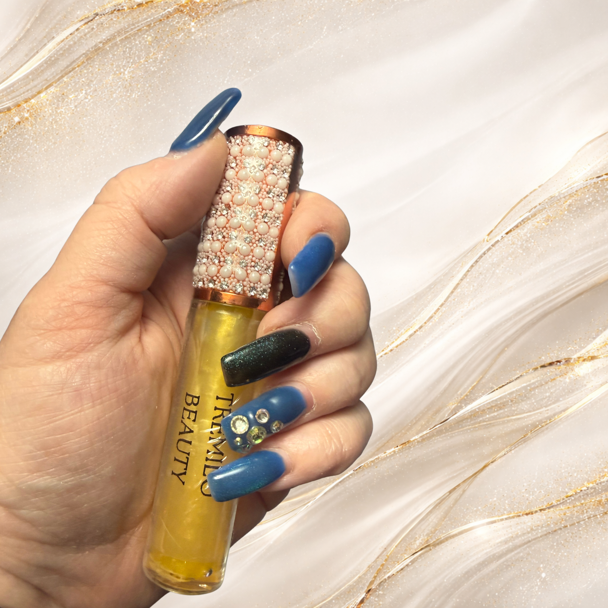 Steel City Gold lip gloss from Tremilo Beauty held in hand featuring gold shimmer gloss and pearl rhinestone cap.