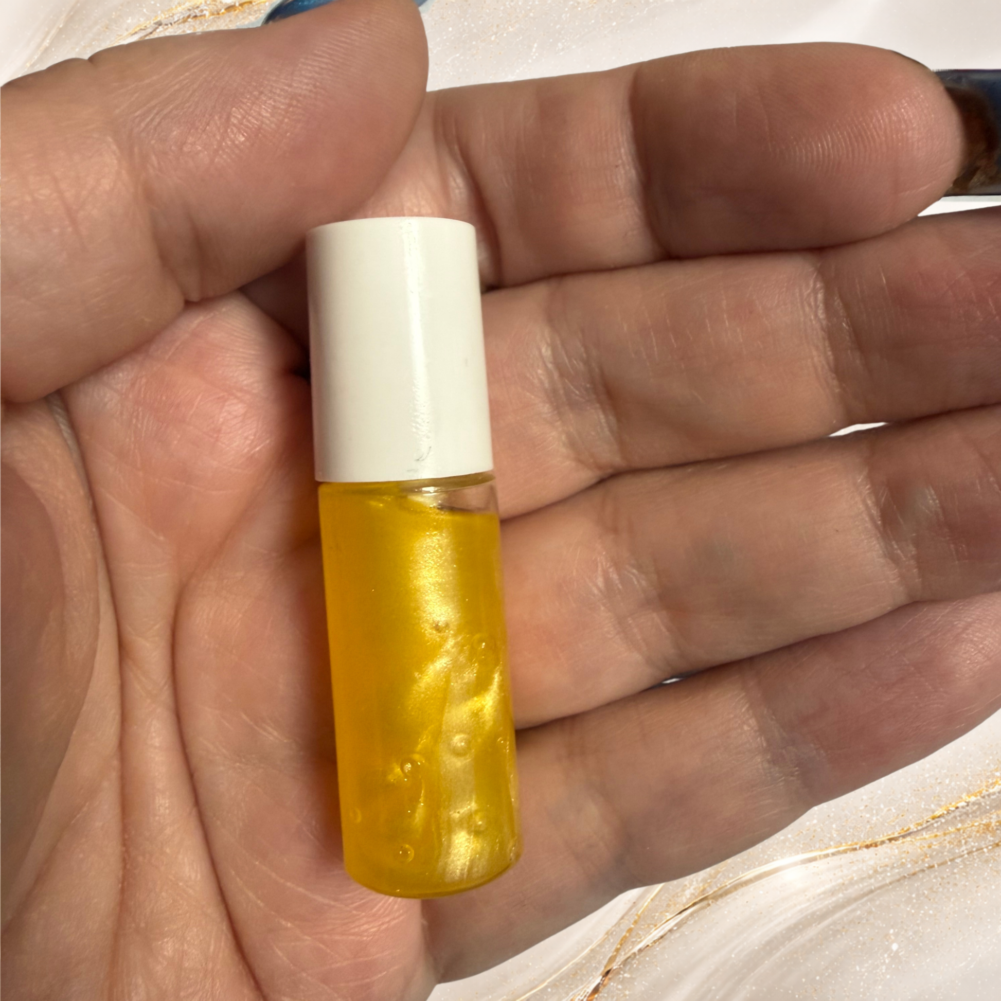 Steel City Gold mini lip gloss sample held in hand featuring gold shimmer gloss in a small sample tube.