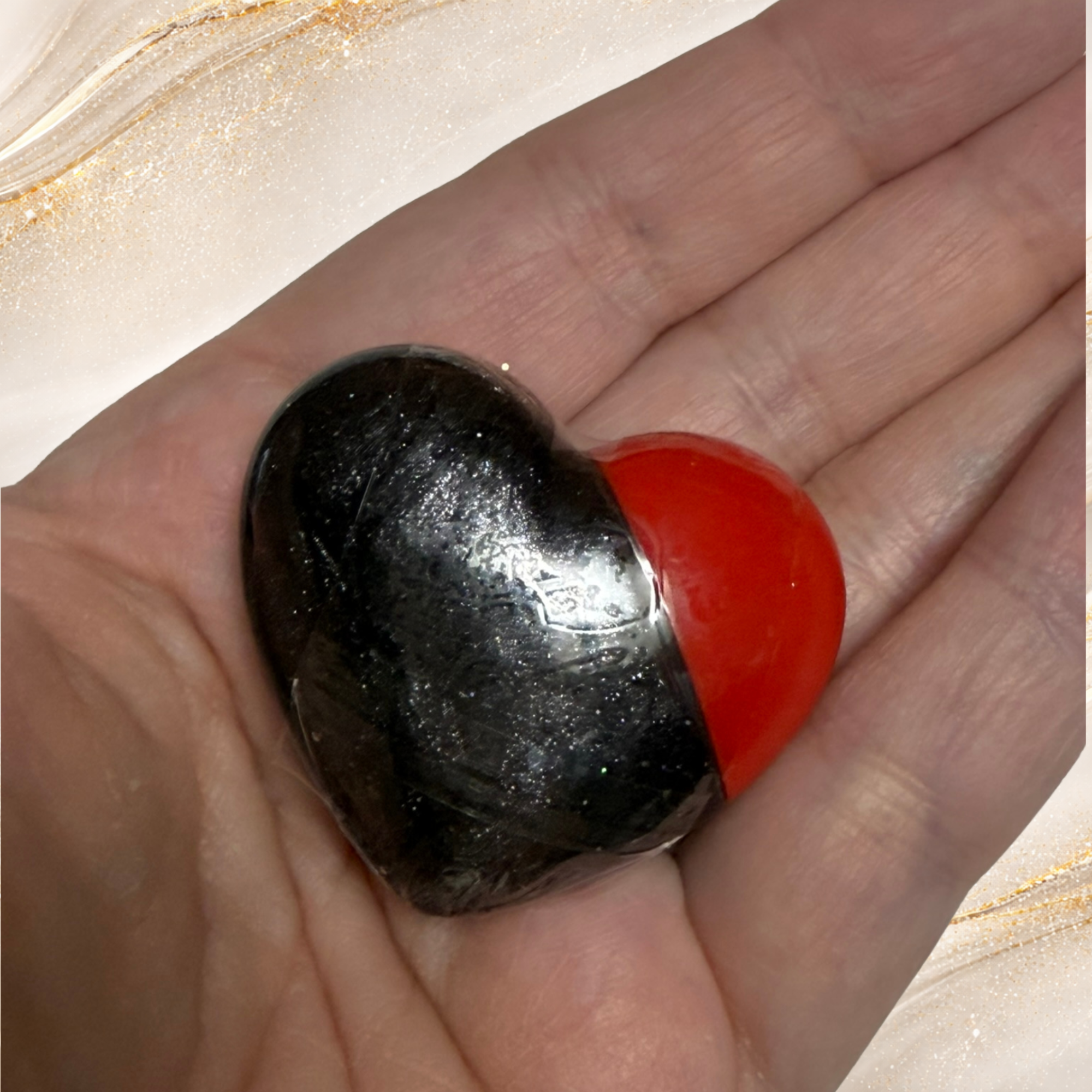 Black Gold heart-shaped gloss from Tremilo Beauty held in hand showing black and red gloss design