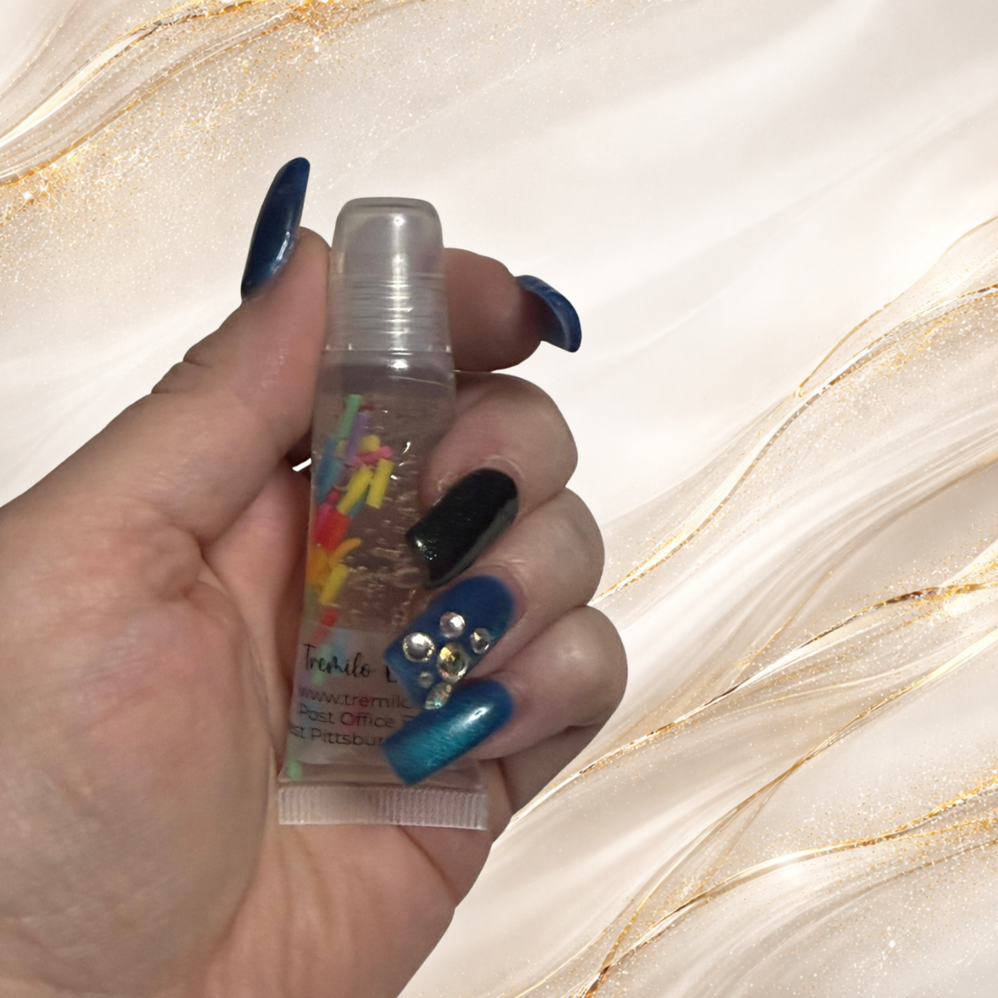Hand holding Tremilo Island Confetti lip gloss squeeze tube with colorful sprinkle confetti inside clear gloss