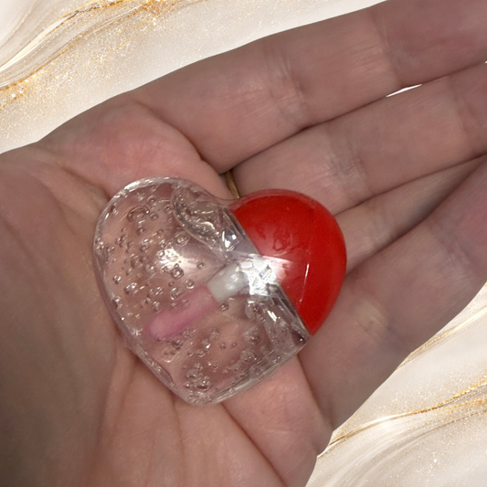Steel Chemistry heart-shaped lip gloss from Tremilo Beauty held in hand showing clear gloss with bubble texture and red heart cap